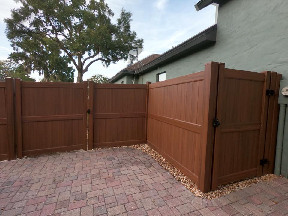 Valla de privacidad de vinilo marrón con portón doble instalada a lo largo del perímetro residencial pavimentado