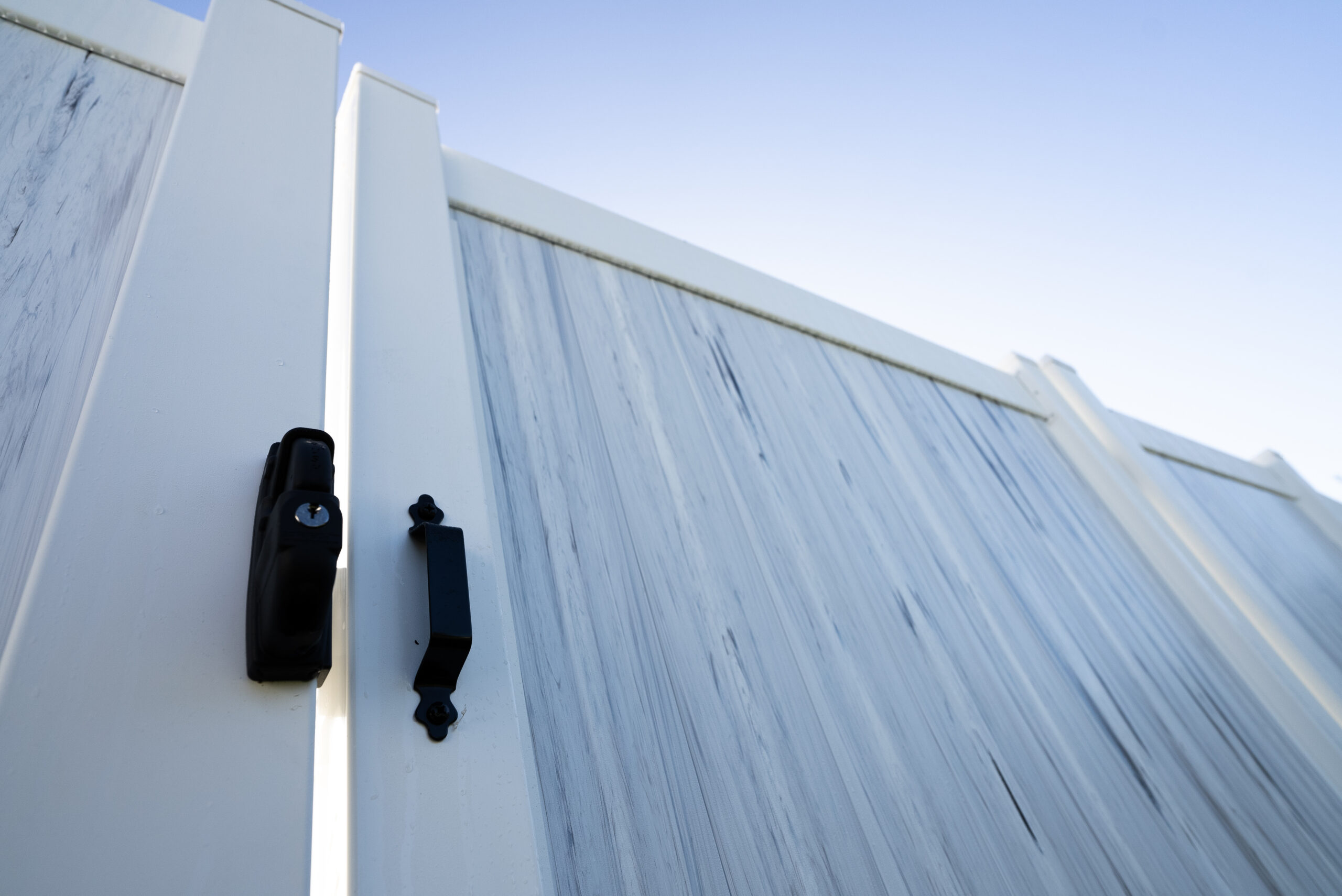Primer plano de una puerta de valla de vinilo blanco con bisagras y herrajes de pestillo de alta resistencia